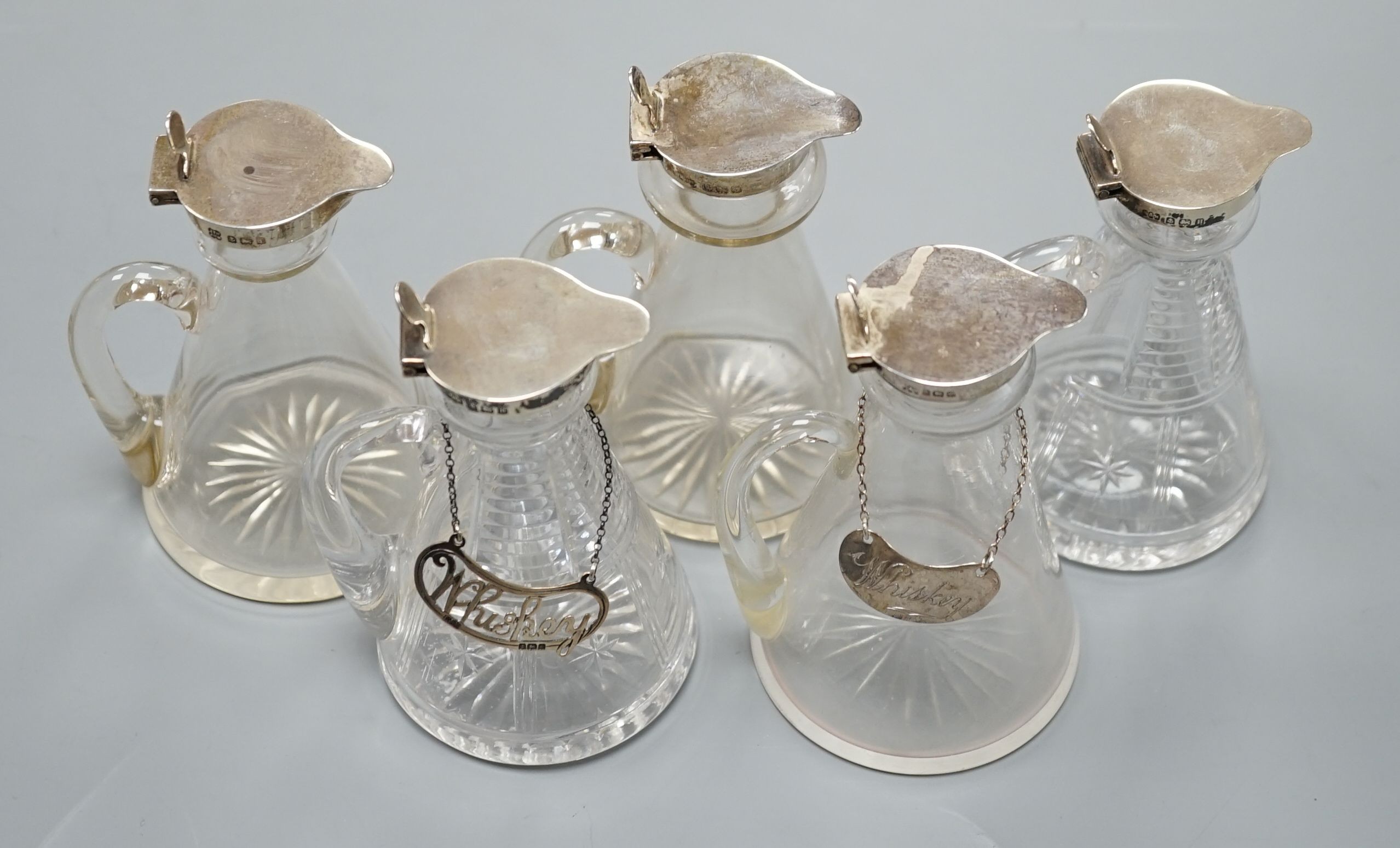 Five early 20th century and later silver mounted glass whisky tot jugs by Hukin & Heath, including a pair, Birmingham 1932, together with two silver Whiskey labels, 11cm.